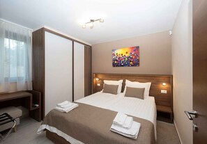 Ein Hotelzimmer mit Bett, Nachttischen, Schreibtisch, Stuhl, einem Gemälde und einer Deckenleuchte.