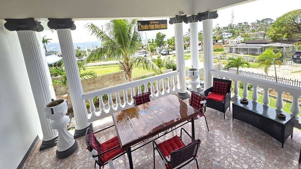 A covered outdoor seating area with a table and chairs, columns, and a view of the surrounding landscape.