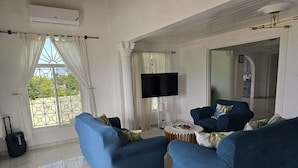 A living room with two blue sofas, a flat-screen TV, and a large window with curtains.