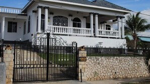 A large, two-story house with a balcony, a stone wall, and a black gate.