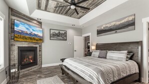 Ein Schlafzimmer mit Kamin, Bett, Deckenventilator und Kunstwerken an den Wänden.