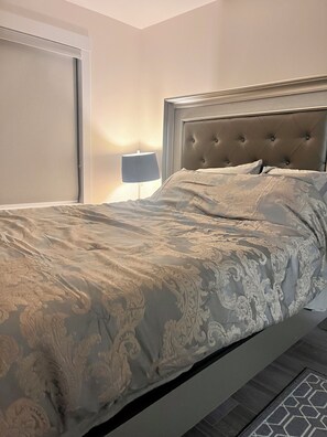 Un lit bien fait, avec une tête de lit capitonnée, une lampe de chevet et une couvre-lit à motifs.