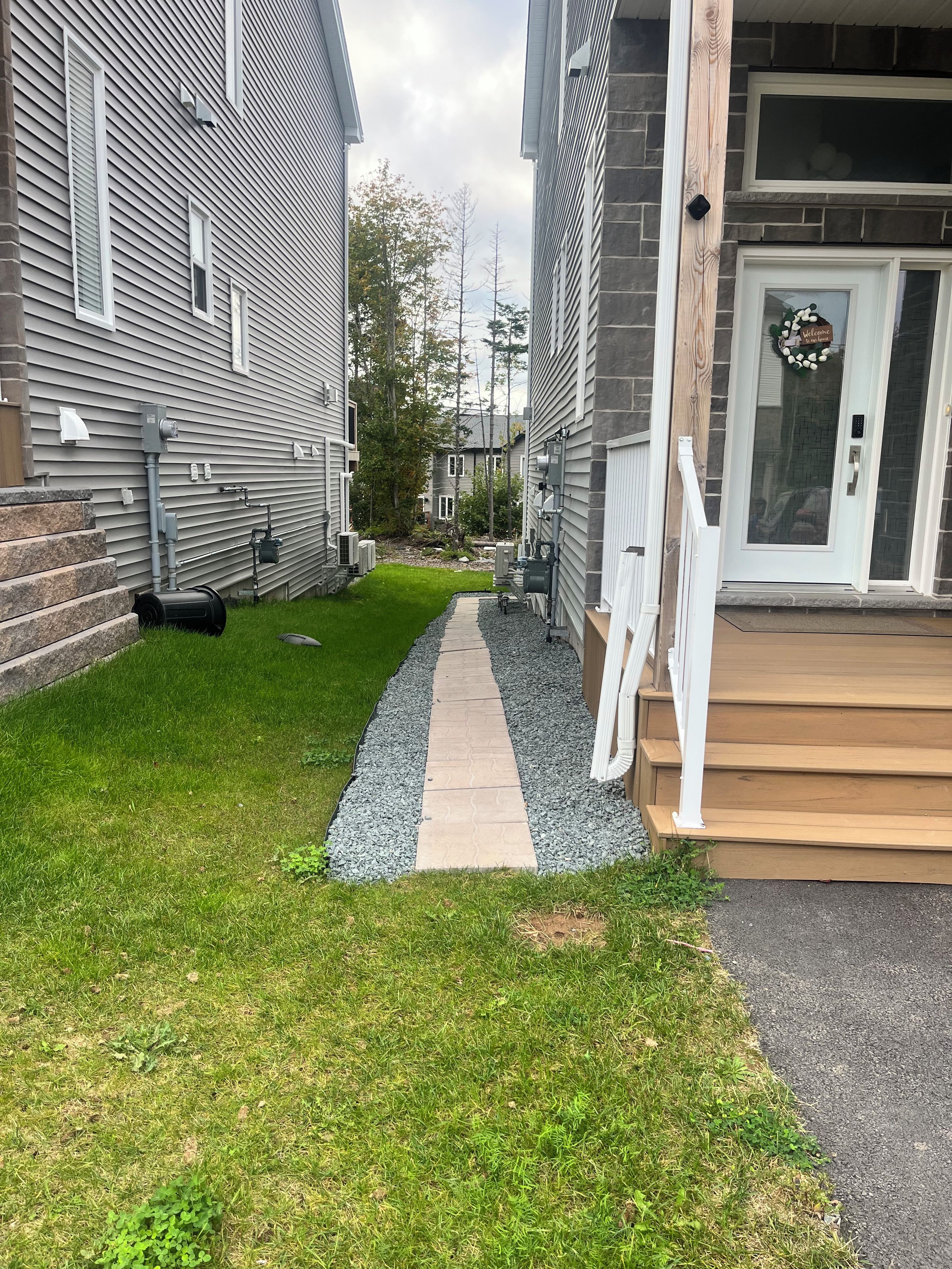 Una propiedad residencial con un sendero pavimentado que conduce a una puerta principal, un pequeño jardín frontal con césped y un muro de piedra.