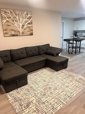 Un sofá modular, un tapete estampado y una zona de cocina con una mesa y sillas.