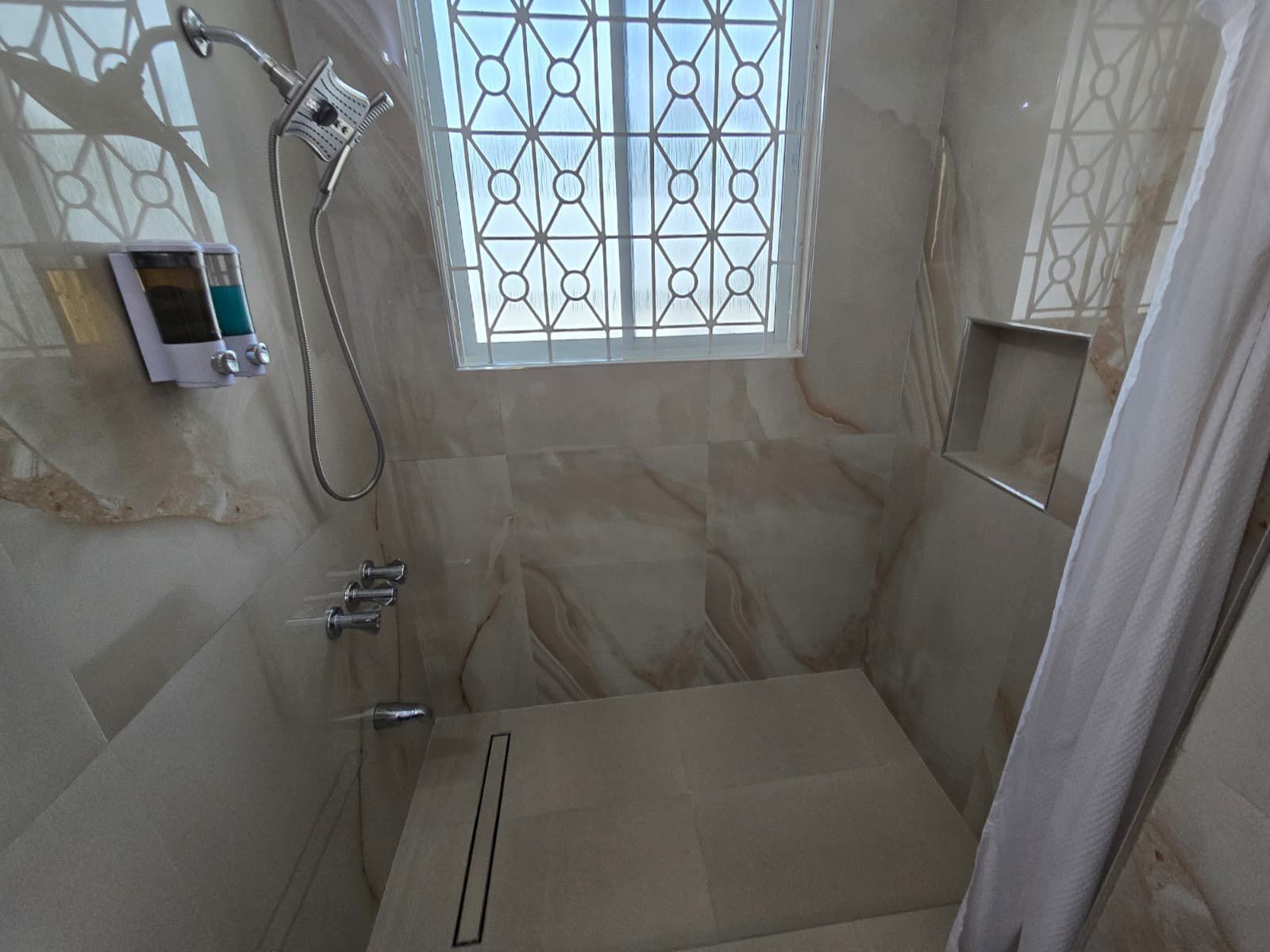 Une salle de bain avec une douche, une fenêtre ornée d’un motif géométrique et un porte-serviettes.