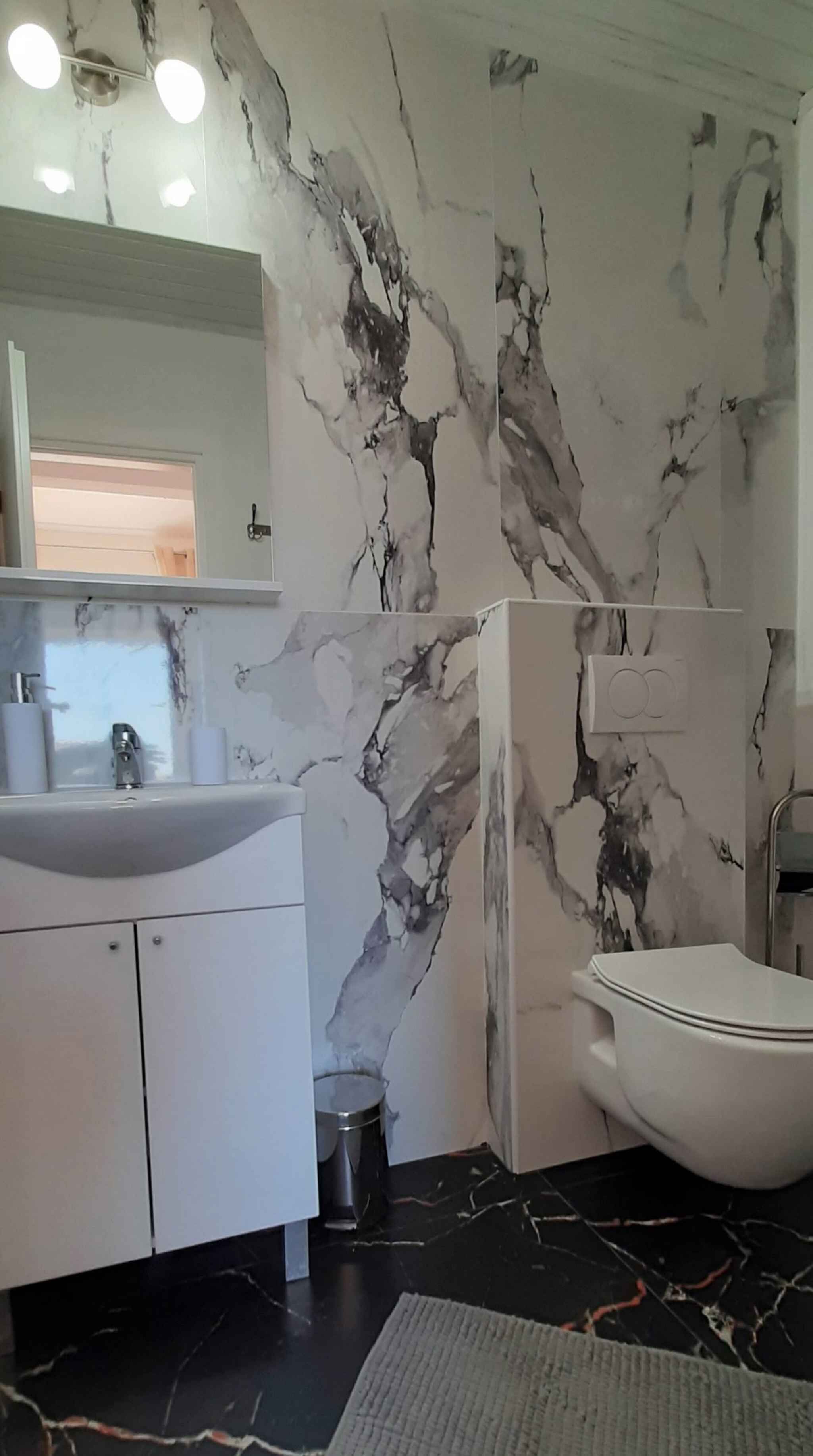 A bathroom with a marble wall, a sink, a toilet, and a mirror.
