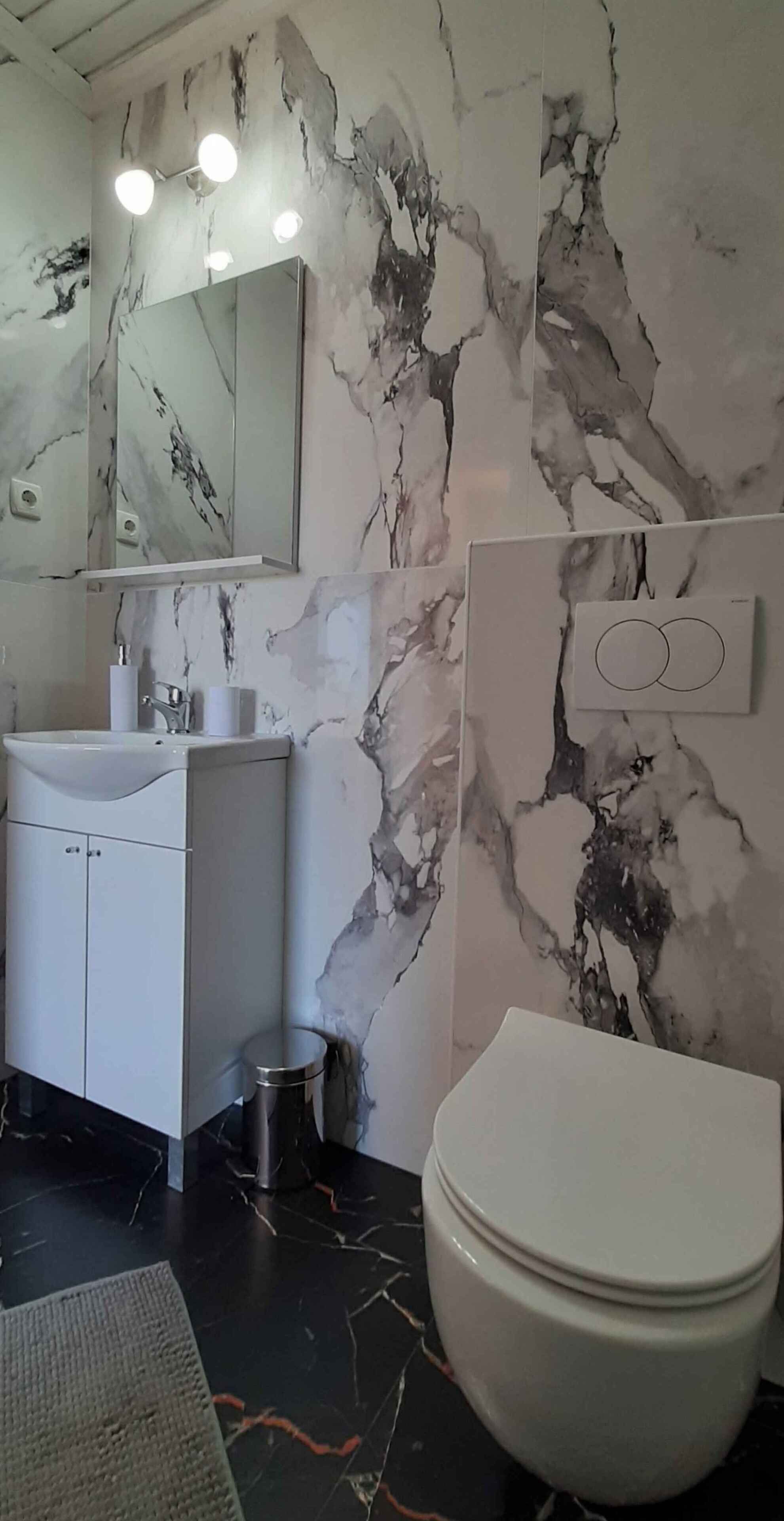 A bathroom with a marble wall, a white sink, a mirror, and a toilet.