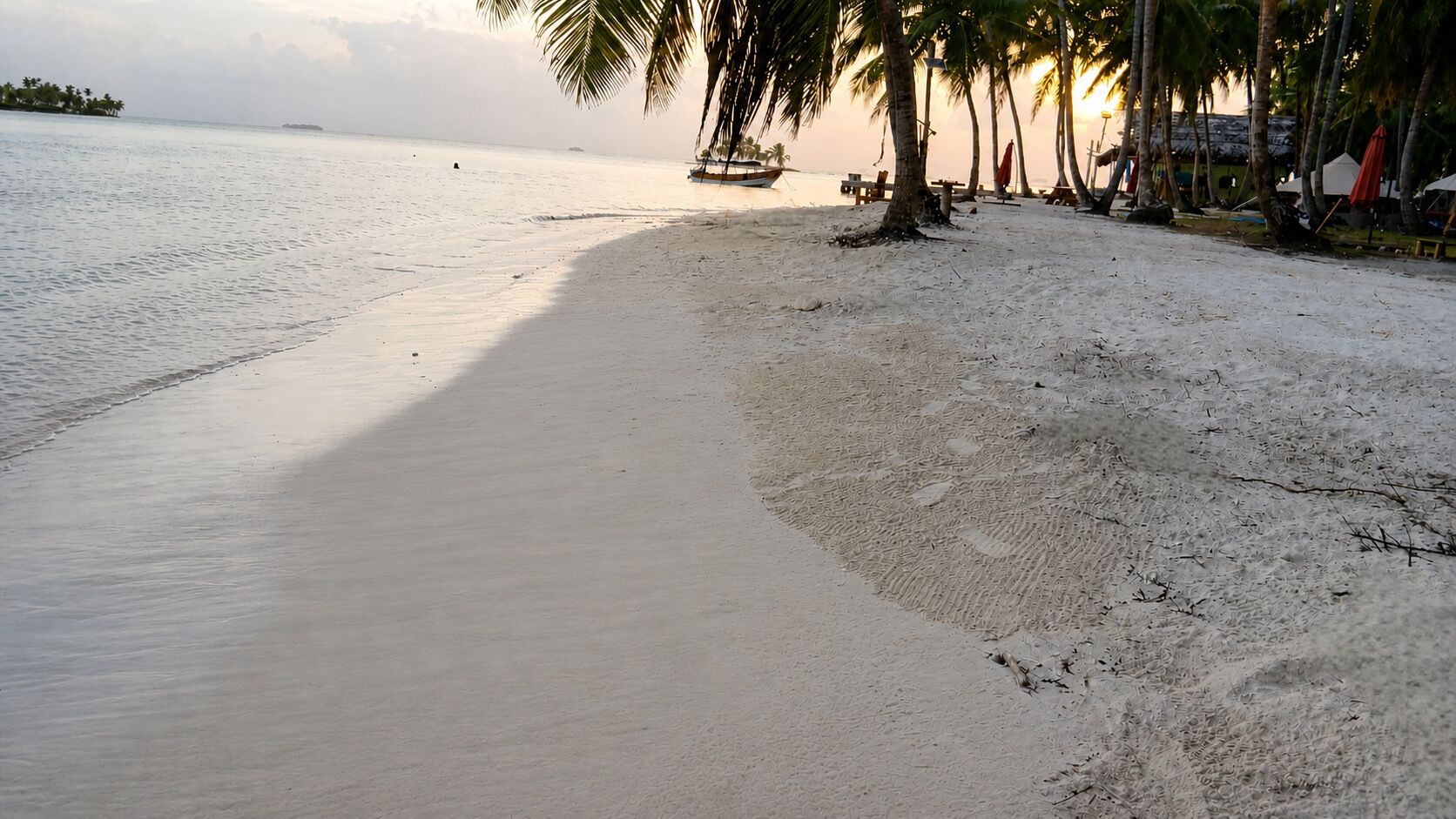Une plage avec un bateau, des palmiers et une île au loin.