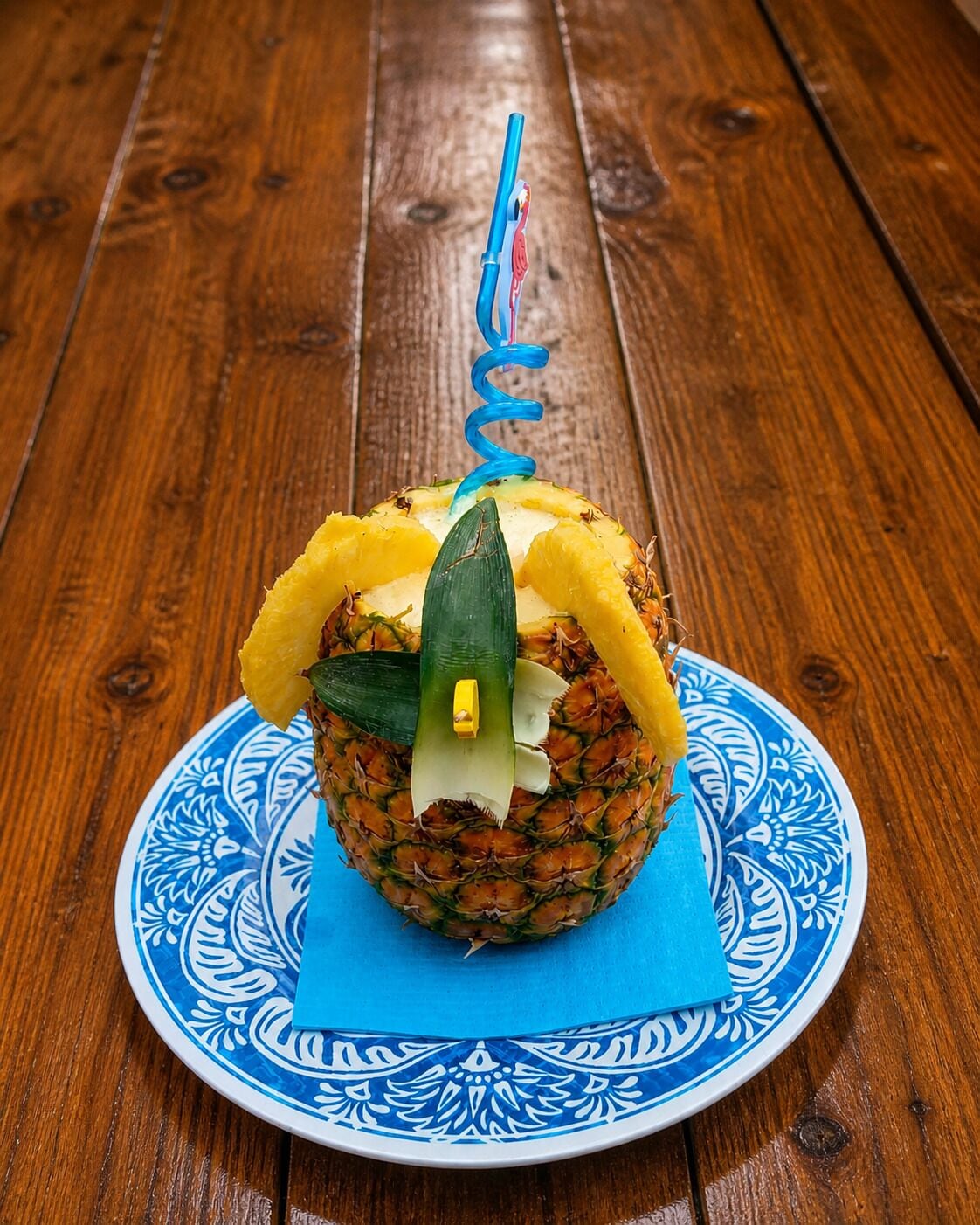 A pineapple on a decorative plate with a blue pattern, placed on a wooden table.