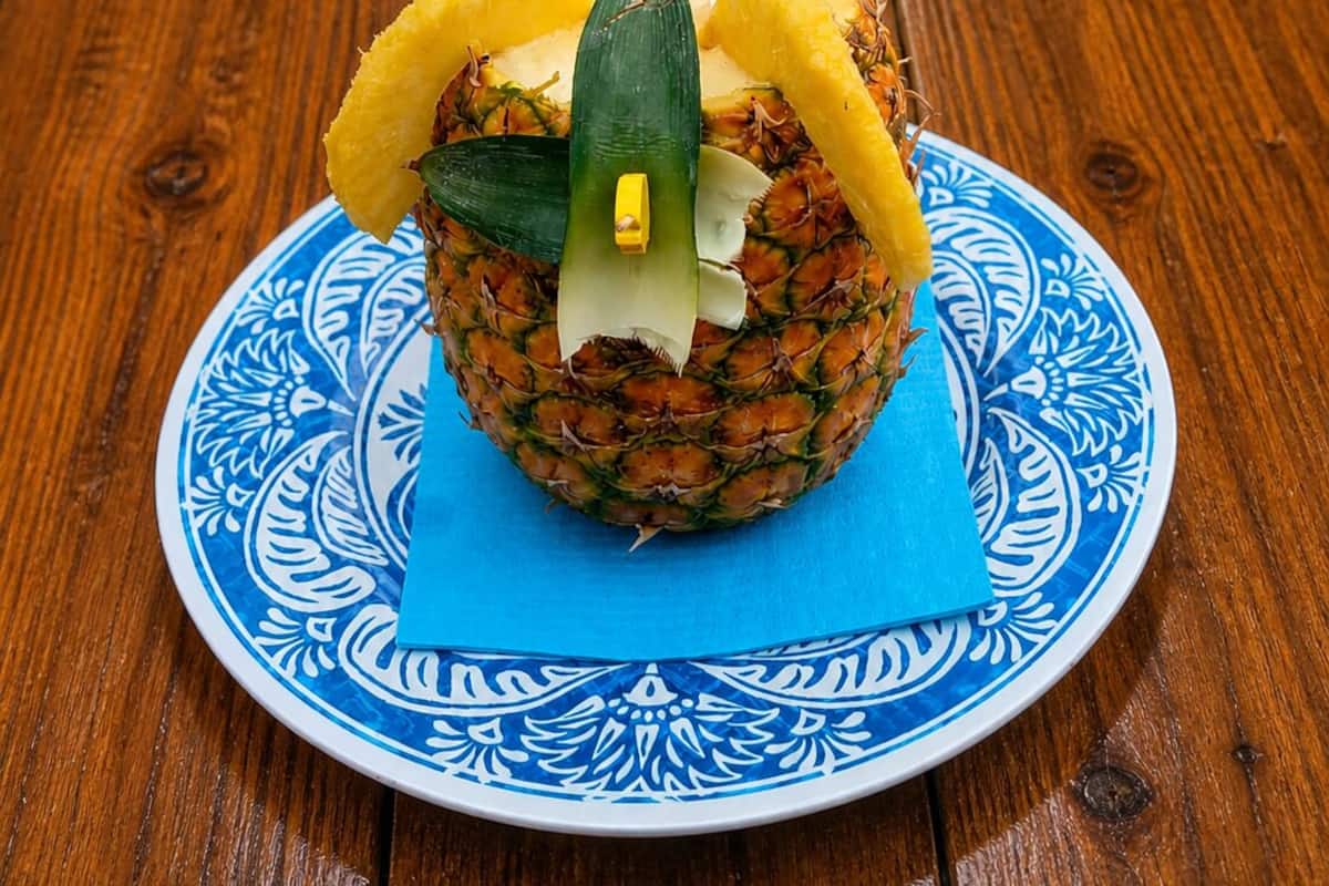 A pineapple on a decorative plate with a blue pattern, placed on a wooden table.