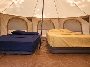 A tent with two beds, one with a blue mattress and the other with a yellow mattress.
