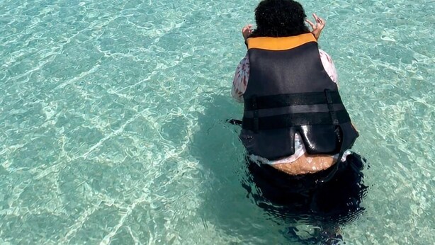 A clear blue sky, a calm sea, and people in the water.