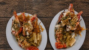 Two plates of lobster with vegetables and pasta on a wooden table.