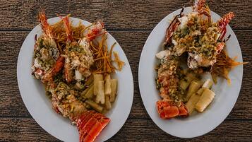 Dos platos de langosta con verduras y pasta sobre una mesa de madera.