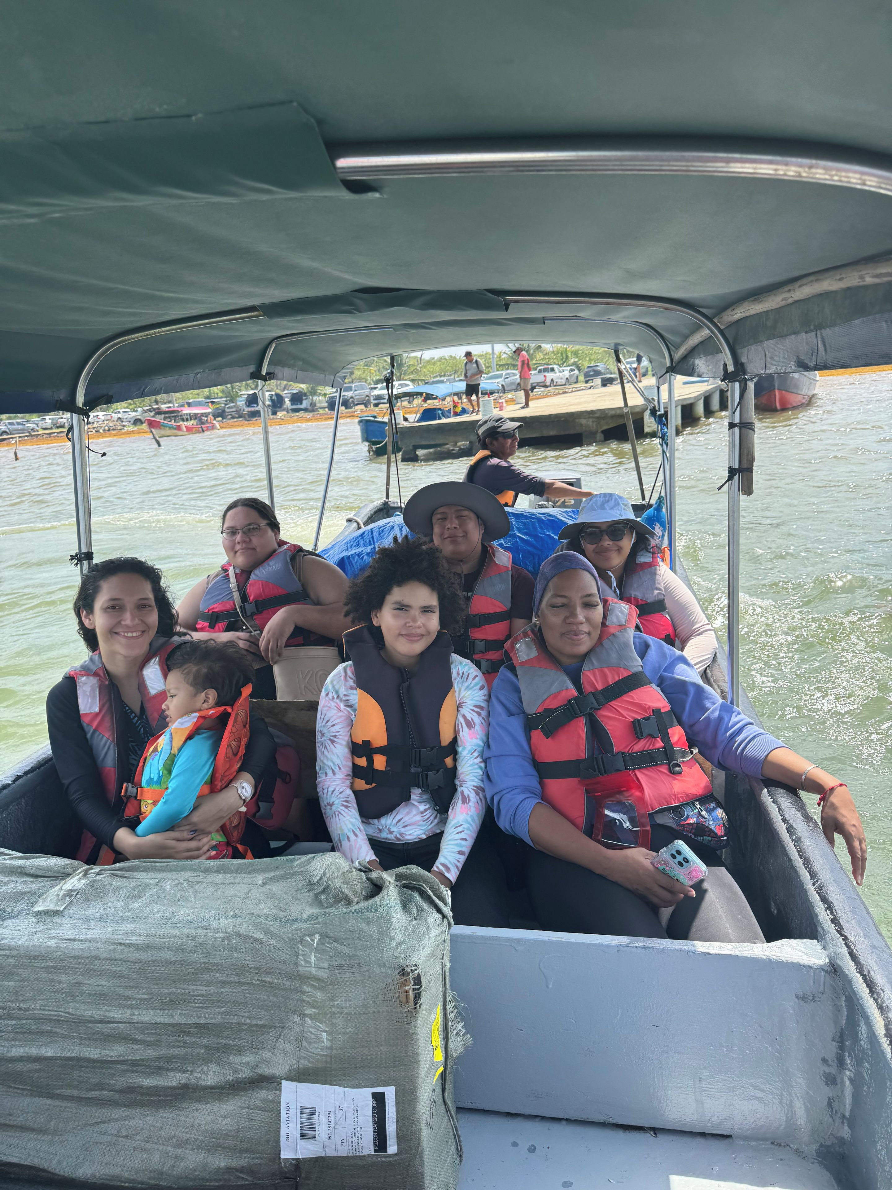 A group of people on a boat with life jackets, a covered area, and a dock in the background.
