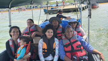 A group of people on a boat with life jackets, a covered area, and a dock in the background.