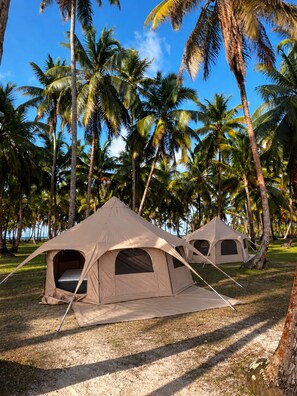 Two beige tents set up on a grassy area with palm trees in the background.
