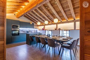 Eine moderne Küche mit integrierten Geräten, ein Essbereich mit großem Tisch und Stühlen sowie eine Holzbalkendecke.