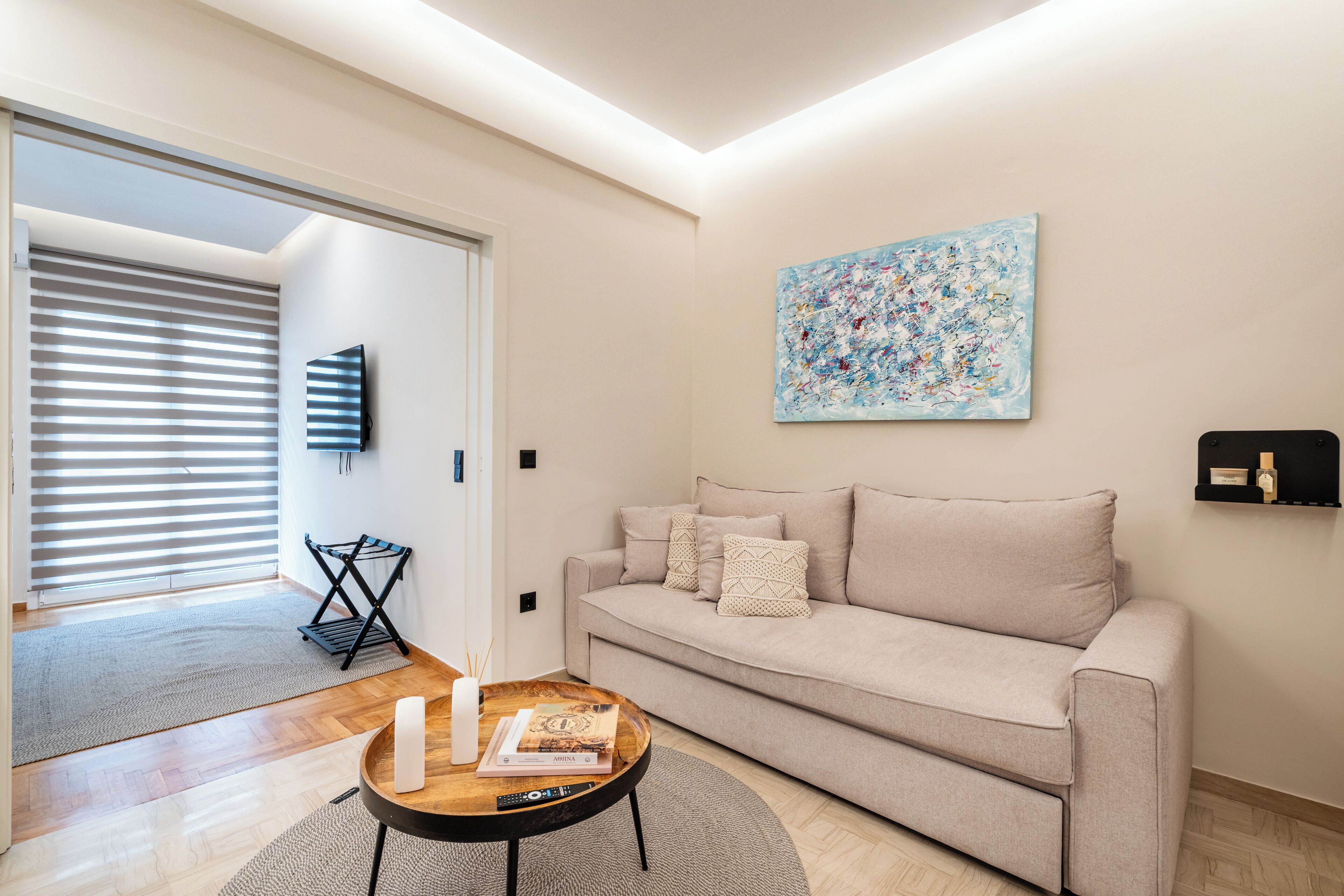 A living room with a sofa, a coffee table, a painting, and a television.