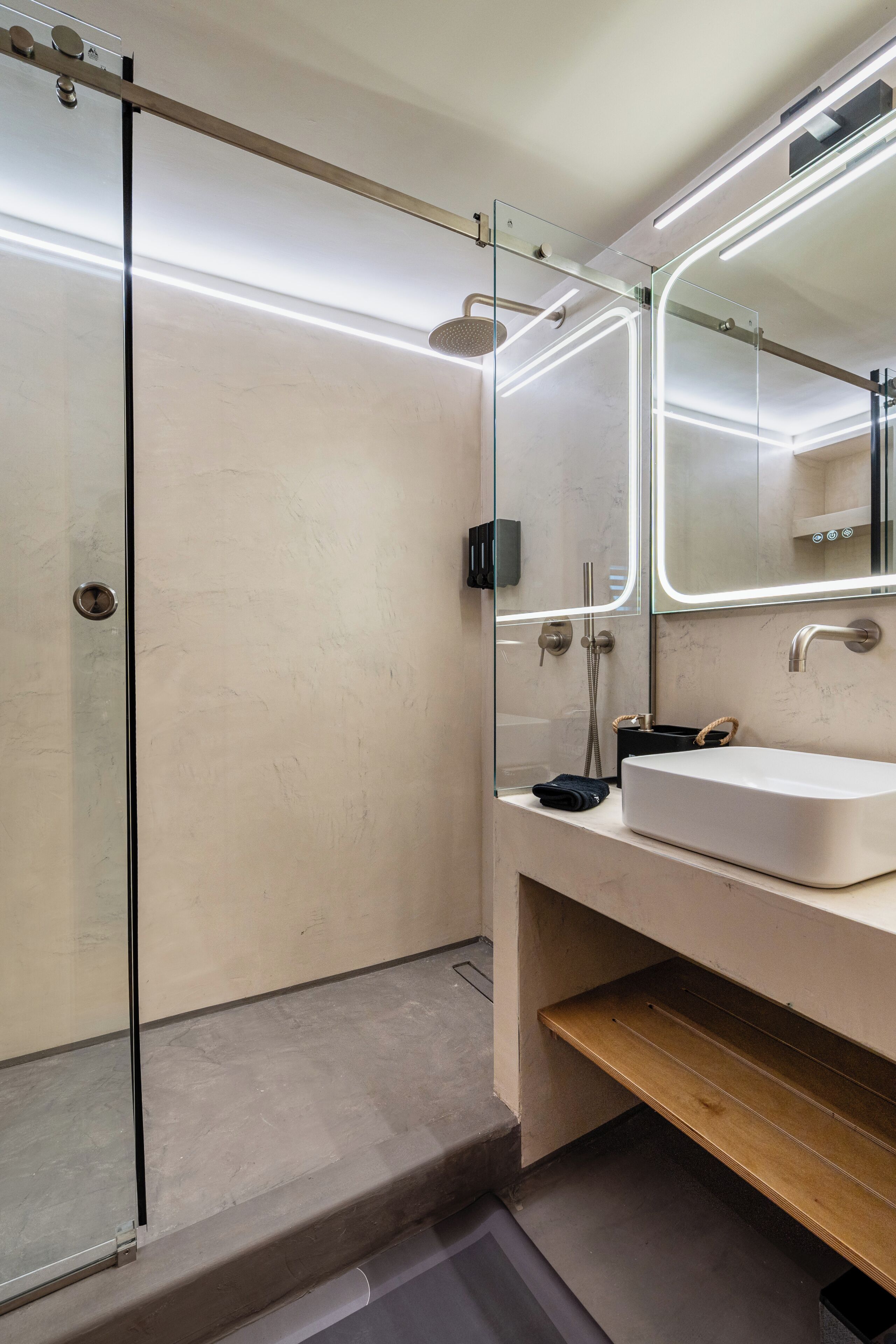 A modern bathroom with a glass-enclosed shower, a white sink, and a mirror with integrated lighting.