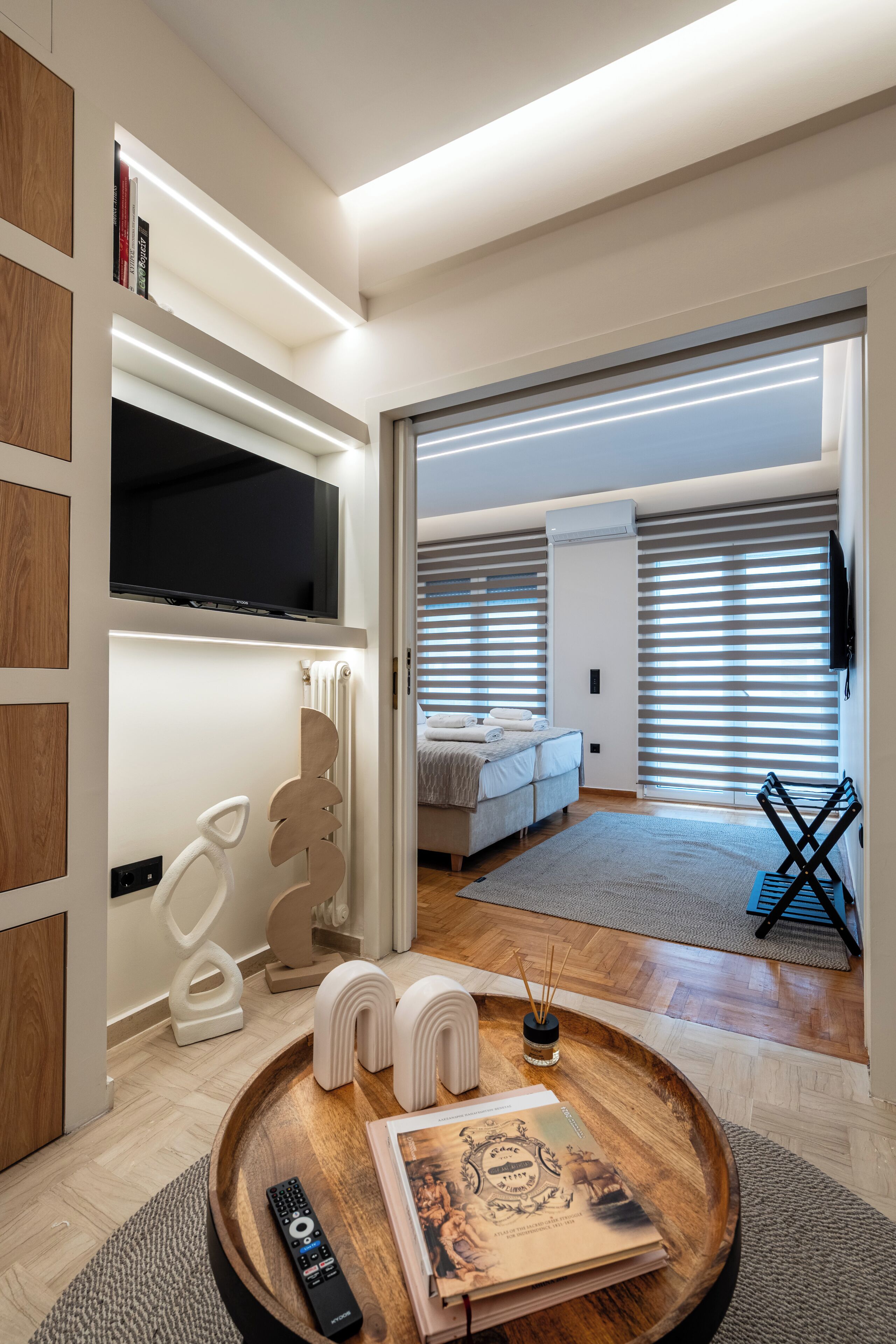 A modern hotel room with a flat-screen TV, a bed, a seating area with a tray table, and a view through the window.