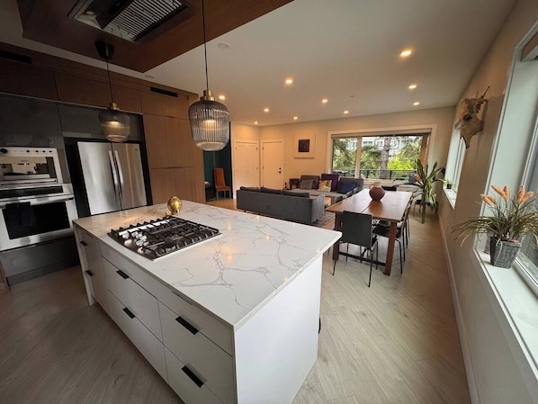 A modern kitchen with a central island, built-in appliances, and a dining area with a view.