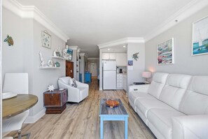A modern living room with a white sofa, a wooden coffee table, and a dining area with a wooden table and chairs. - Oceanfront Balcony Views • Bright Studio • Clean & Great Value (Daytona Beach)
