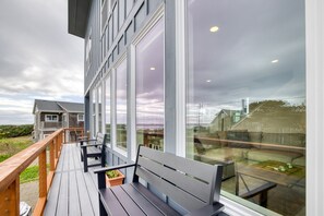A wooden deck with benches, large windows, and a view of a house and landscape. - Sea View-Brand new! Steps to beach, great views, open & spacious. (Cloverdale)