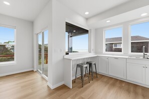 A modern kitchen with white cabinetry, a large window, and a sliding glass door. - Sea View-Brand new! Steps to beach, great views, open & spacious. (Cloverdale)