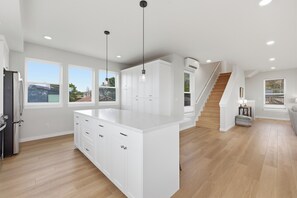 A modern kitchen with white cabinets, a central island, pendant lighting, a staircase, and large windows. - Sea View-Brand new! Steps to beach, great views, open & spacious. (Cloverdale)