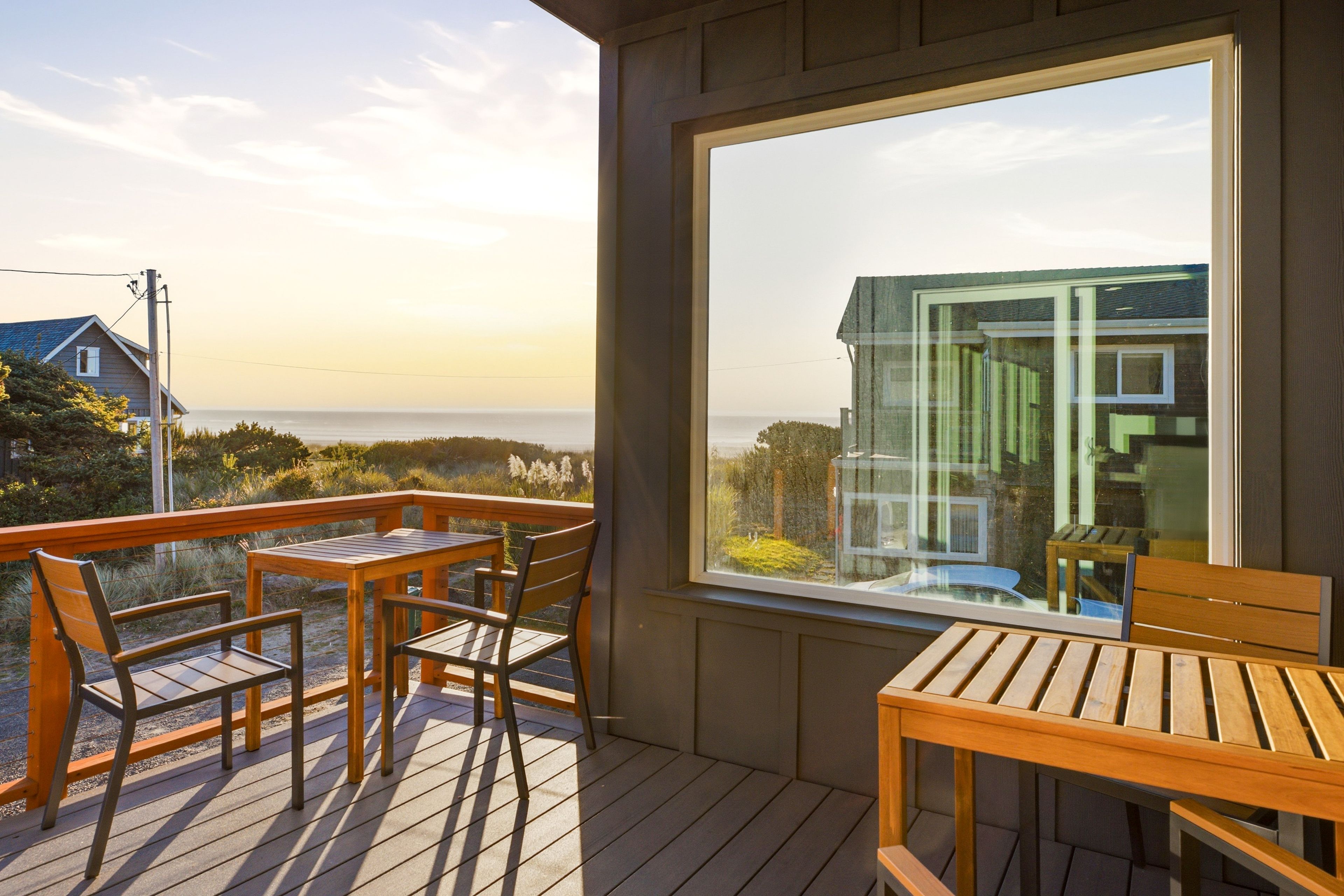 A wooden deck with a table and chairs, overlooking a body of water and a distant shoreline.