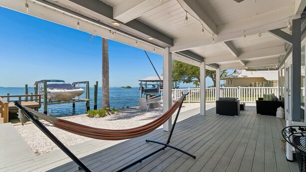 A covered deck with a hammock, outdoor seating, and a view of the water.