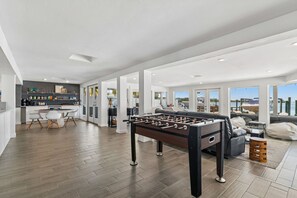 A spacious living area with a foosball table, a kitchen with a bar, and large windows offering a view of the water. - Sunset Waterfront Paradise | Kayaks, Dock, + Views (Palm Harbor)
