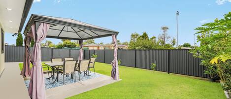 A patio with a covered seating area, a lawn, and a fence.