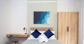 A hotel room with a bed, a desk, a chair, a wardrobe, and a painting on the wall. - Modern 6BR Sunderland Home | Sleeps 12 | Parking (Tyne and Wear)