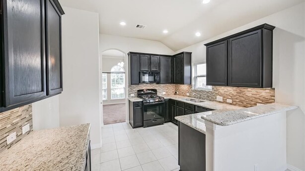 A modern kitchen with dark cabinetry, granite countertops, and a central island. - Katy Brick Haven (Katy)