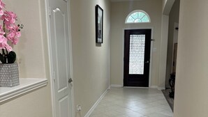 A hallway with a tiled floor, a white door, a framed picture on the wall, and a window with a decorative design. - Katy Brick Haven (Katy)