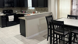 A modern kitchen with black cabinets, a granite countertop, and a dining area with a table and chairs. - Katy Brick Haven (Katy)