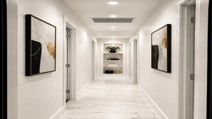 A hallway with white marble flooring, white walls, and framed artwork on both sides.