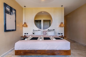 A bedroom with a large bed, two bedside tables, a round mirror above the bed, and two hanging lamps. - Oceanfront Luxury Condo in Bahia Soliman | Swimming Pool + Spectacular View (Tankah Cuatro, Tulum)