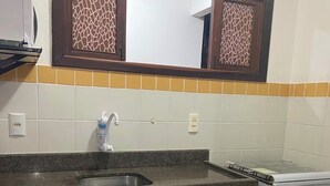 Una cocina con encimera de granito, pileta de acero inoxidable, estufa blanca, armarios de madera y un espejo decorativo con diseño geométrico.