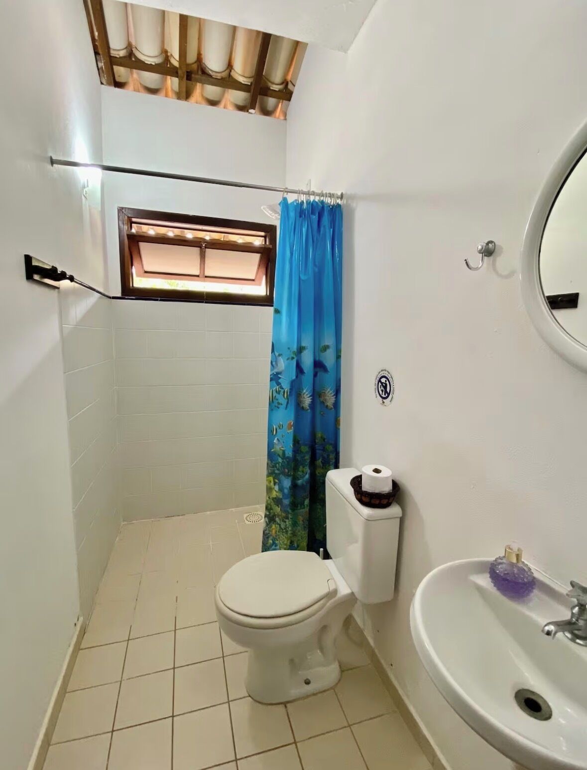A small bathroom with a toilet, a sink, a shower curtain, and a window.