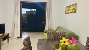 Un salón con una mesa de madera oscura, sillas de mimbre, un sofá y un televisor sobre un mueble.