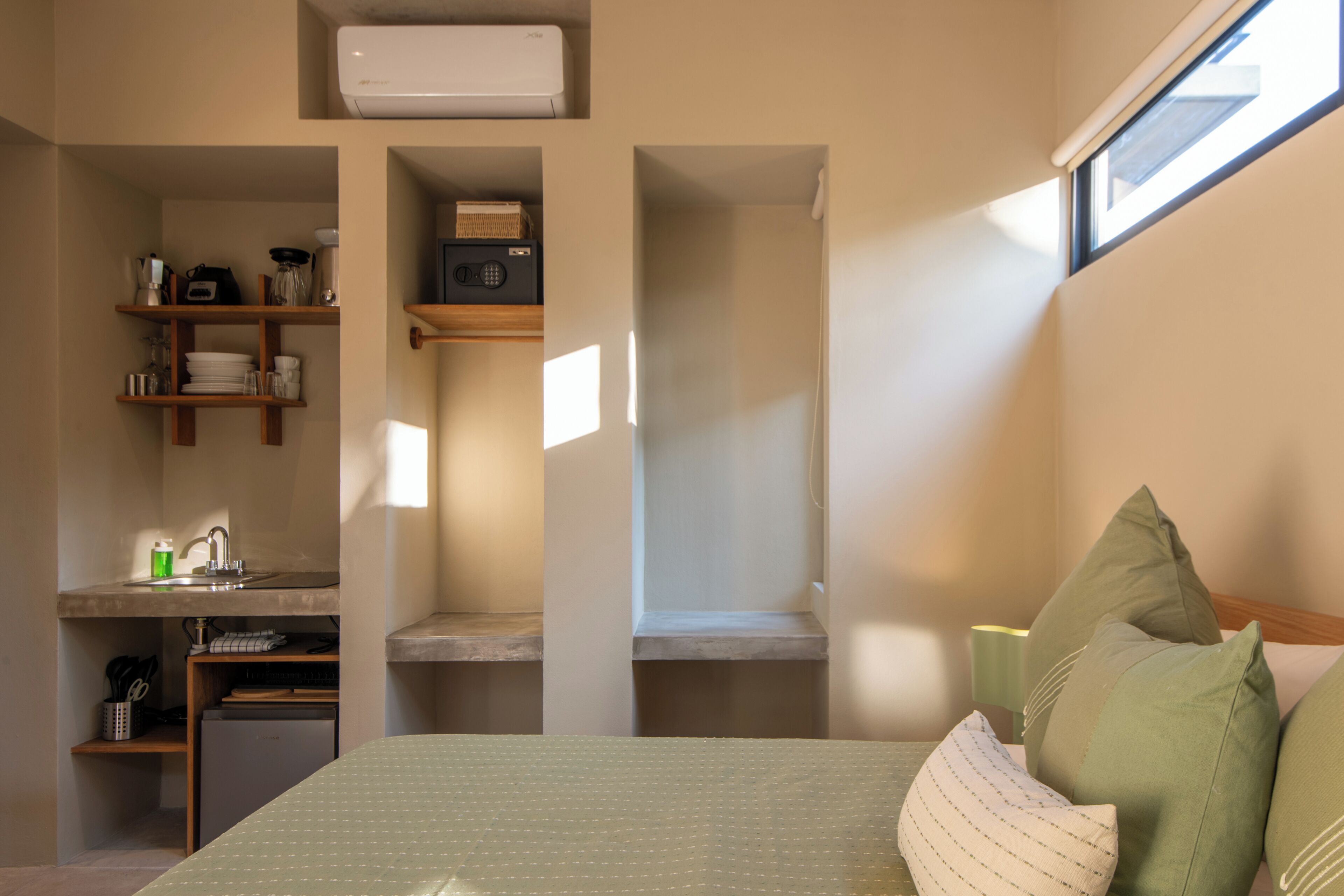 A bedroom with a bed, a window, and built-in shelves with kitchen items.