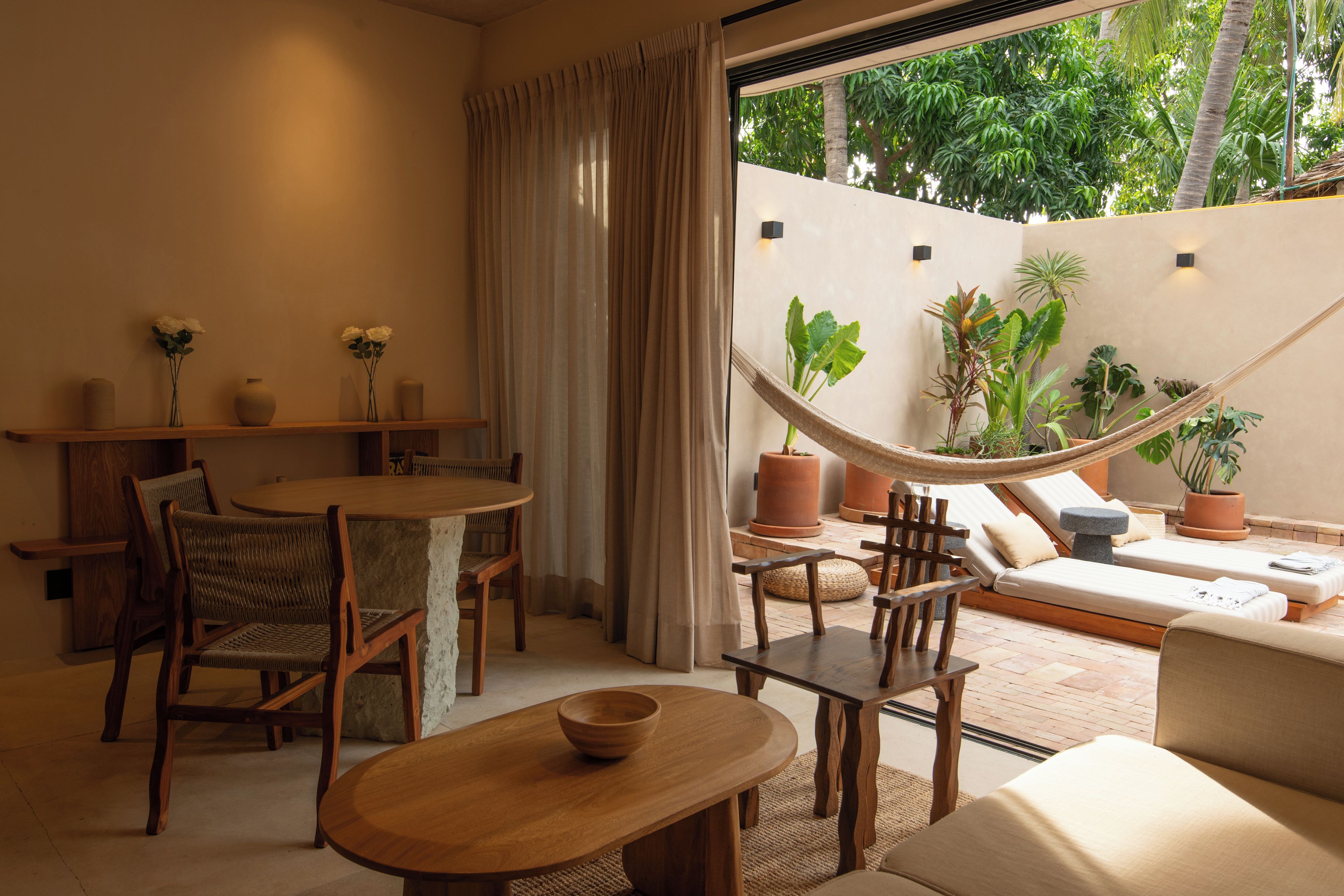 A cozy indoor space with a dining area, a hammock, and a seating area with a view of lush greenery outside.