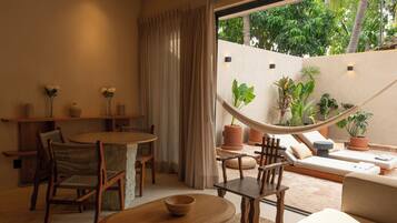 A cozy indoor space with a dining area, a hammock, and a seating area with a view of lush greenery outside.