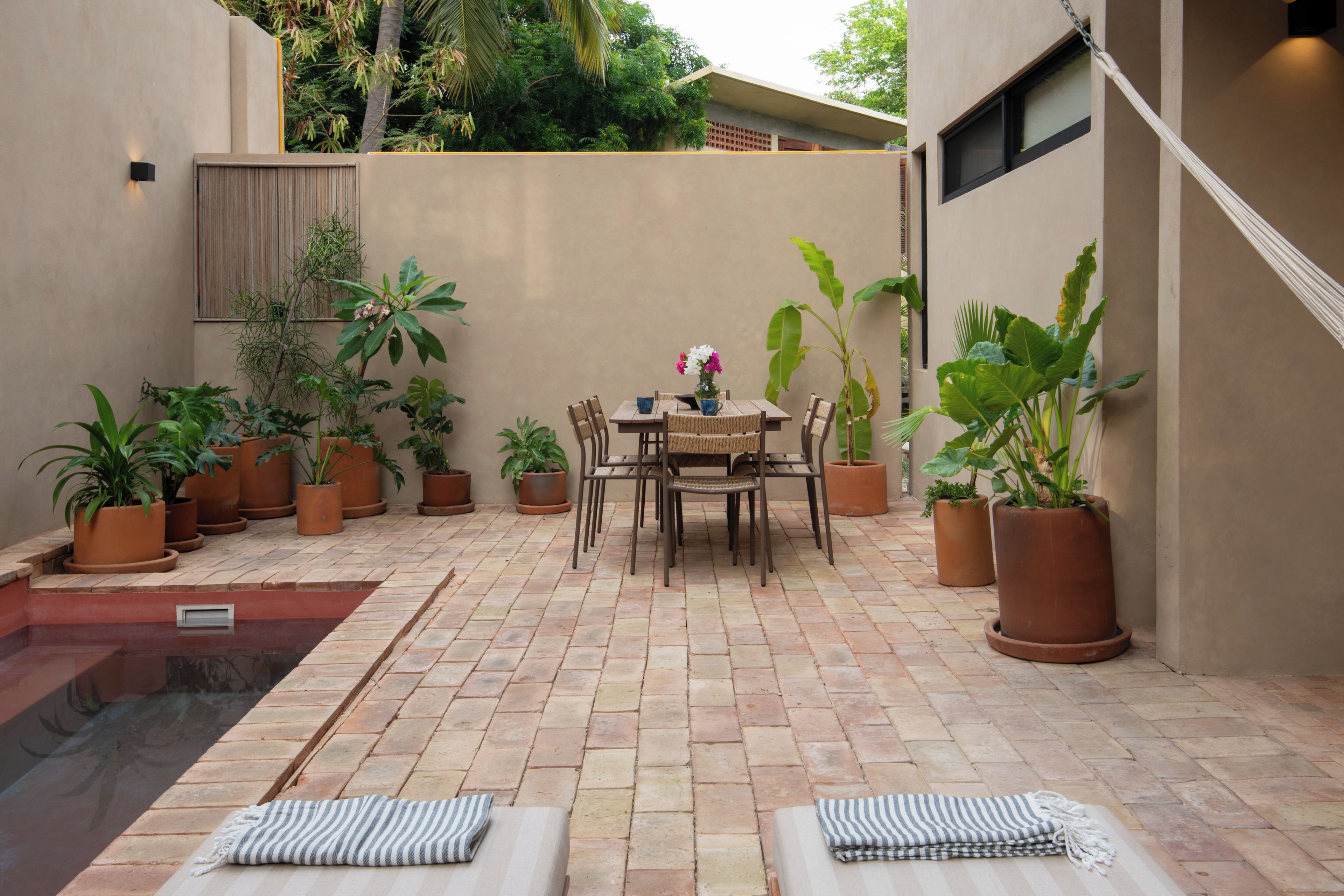 A patio with a pool, a table with chairs, and potted plants.