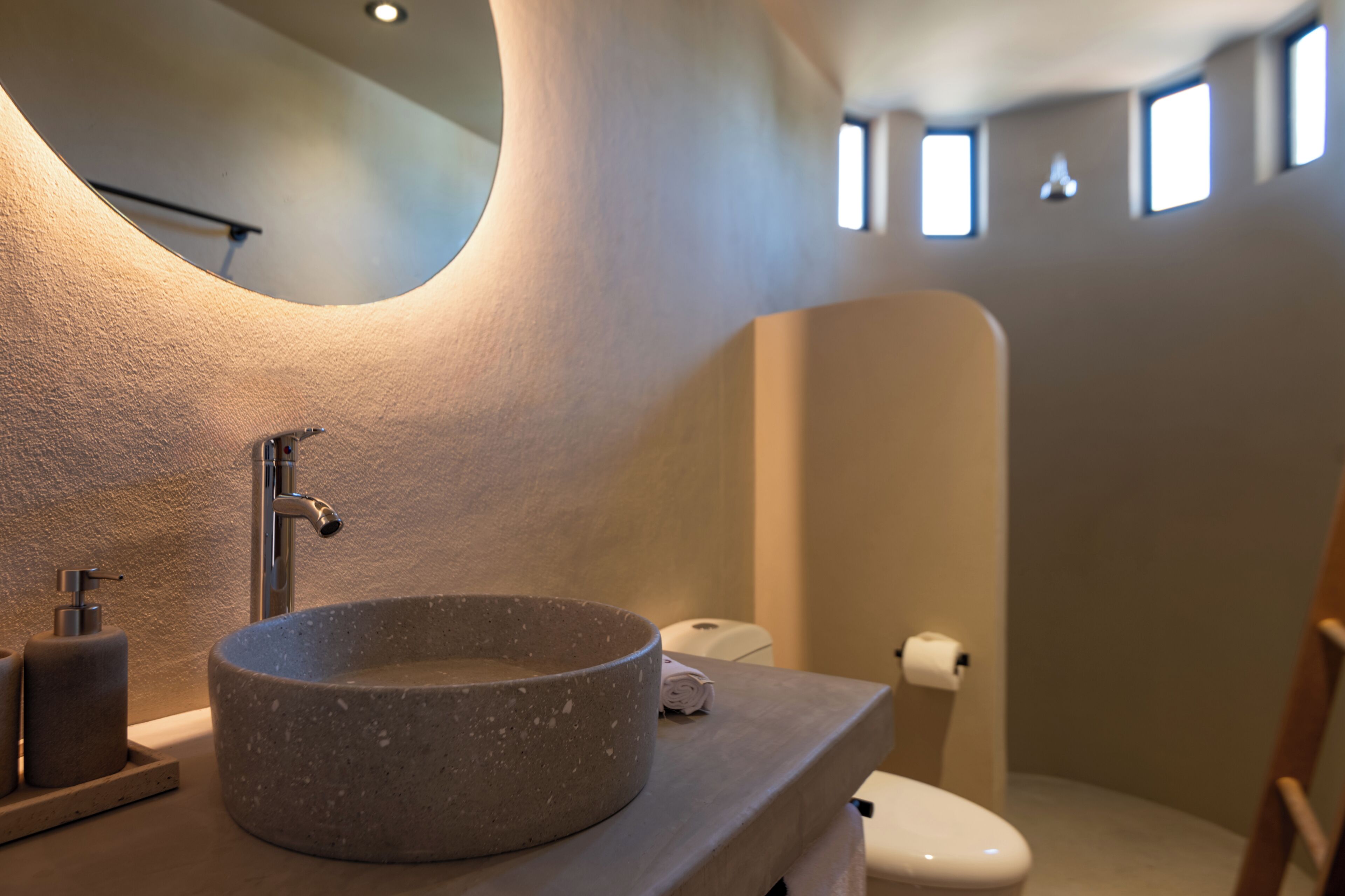 Un baño con un lavamanos de piedra redonda, un inodoro y un espejo.