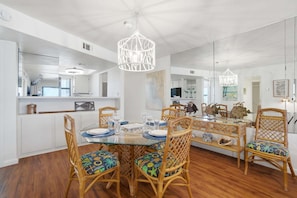 A dining area with a glass table, wicker chairs, and a hanging light fixture. - Villa Del Mar | Beachfront, Pool, Sunset Views, Sleeps 4 (Fort Myers Beach)