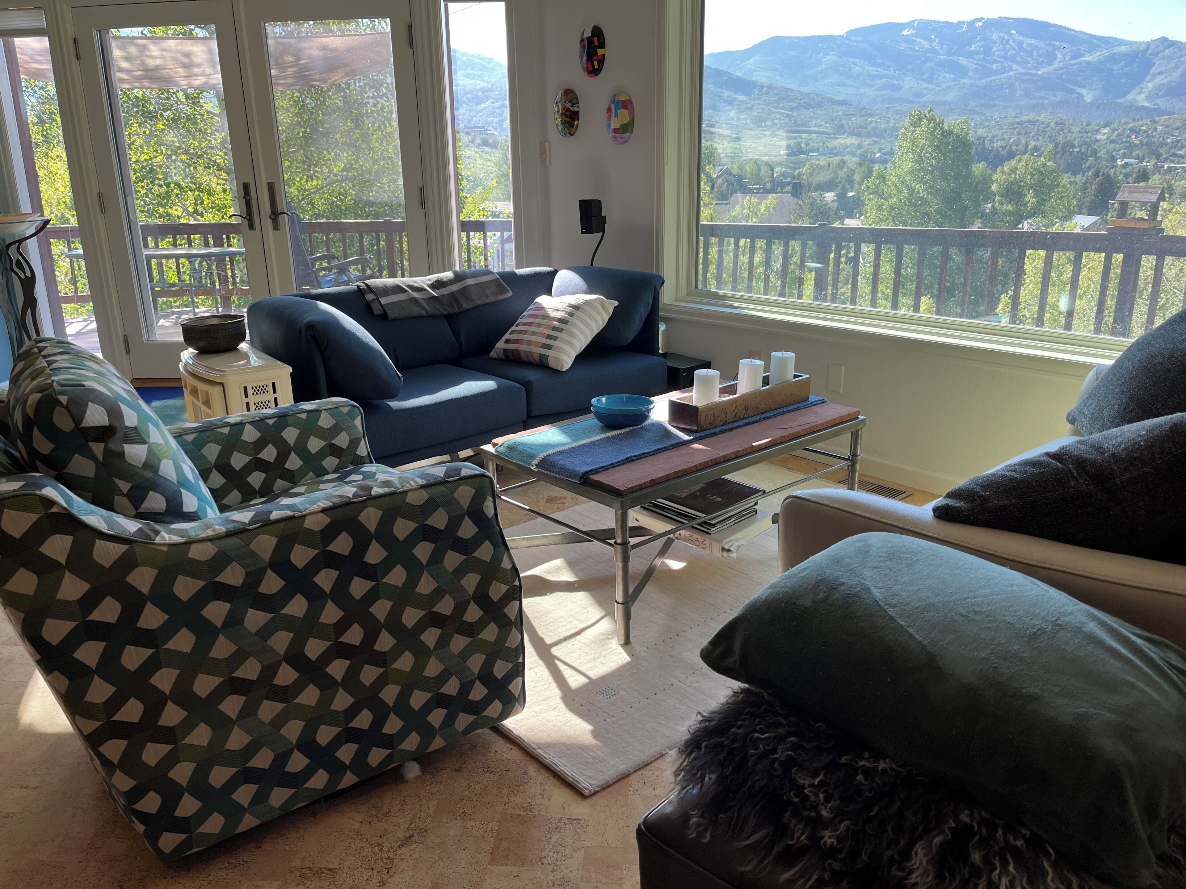 A living room with a blue sofa, patterned armchair, and a view of mountains through large windows.